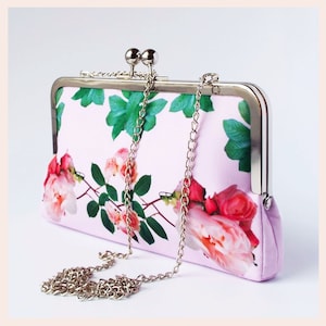 May include: A pink satin clutch with a silver chain strap and a floral print of pink roses and green leaves.