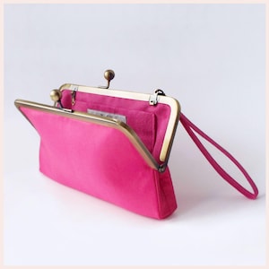May include: A bright pink clutch purse with a gold-toned frame and a small handle. The purse is open, revealing a suede lining.