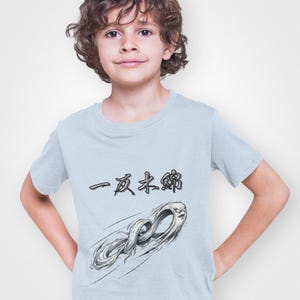 May include: A light blue t-shirt featuring Japanese text and a stylized illustration of a ghostly figure. The graphic is in shades of gray and black. The shirt is made of a soft material.