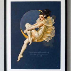 Puede incluir: Impresi&oacute;n art&iacute;stica enmarcada que representa a una mujer sentada con un vestido y guantes color crema, descansando sobre una luna creciente sobre un fondo azul oscuro. Incluye una cita de Mary Shelley.