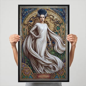 May include: A framed art print featuring a stylized portrait of a woman in a white gown and elaborate hairstyle. The artwork has a gothic theme with French text and ornate stained-glass-style detailing in gold, blue, and green. The print is held by a person.