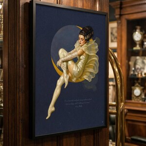 Puede incluir: Impresi&oacute;n art&iacute;stica enmarcada que representa a una mujer con un vestido amarillo sentada en una luna creciente sobre un fondo azul oscuro. La obra de arte tiene un estilo vintage, con una cita en la parte inferior. El marco es negro y la impresi&oacute;n est&aacute; montada en una pared de madera.