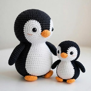 Op de afbeelding: Twee gehaakte pinguïn knuffels. De pinguïns zijn zwart en wit met oranje snavels en voeten. De grotere pinguïn is ongeveer 20 cm hoog en de kleinere pinguïn is ongeveer 10 cm hoog. De pinguïns hebben zwarte ogen en zijn gemaakt van garen.