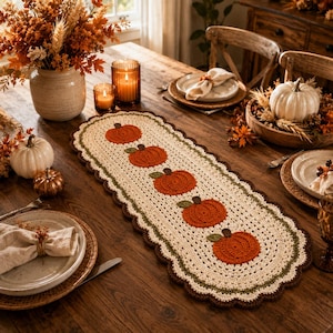 Peut inclure: Un chemin de table ovale en crochet orné de cinq citrouilles orange avec des tiges vertes alignées. Le chemin présente un centre crème, une bordure vert foncé et un bord festonné marron foncé, formant une pièce textile décorative.