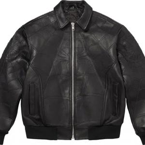 K&ouml;nnte beinhalten: Eine schwarze Leder-Bomberjacke mit einem tonalen, gepr&auml;gten Spinnennetz-Muster auf der Vorderseite und den &Auml;rmeln. Die Jacke verf&uuml;gt &uuml;ber einen klassischen Kragen, einen silberfarbenen Frontrei&szlig;verschluss aus Metall, zwei Seitentaschen sowie schwarze Rippstrickb&uuml;ndchen an &Auml;rmeln und Saum.