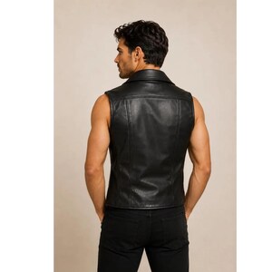 May include: A black sleeveless leather vest featuring a wide collar, vertical seam detailing on the back, and a fitted silhouette. The garment is worn over black trousers, showcasing a smooth texture and a clean, structured design throughout.