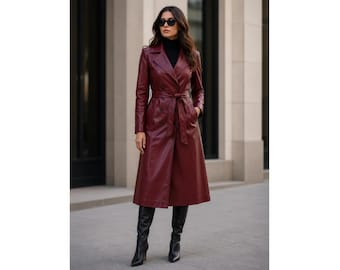 May include: A long, deep burgundy trench coat made of a smooth, leather-like material. The coat features a wide notched collar, long sleeves, and a matching tie belt at the waist. It is worn over a black turtleneck and paired with black boots.