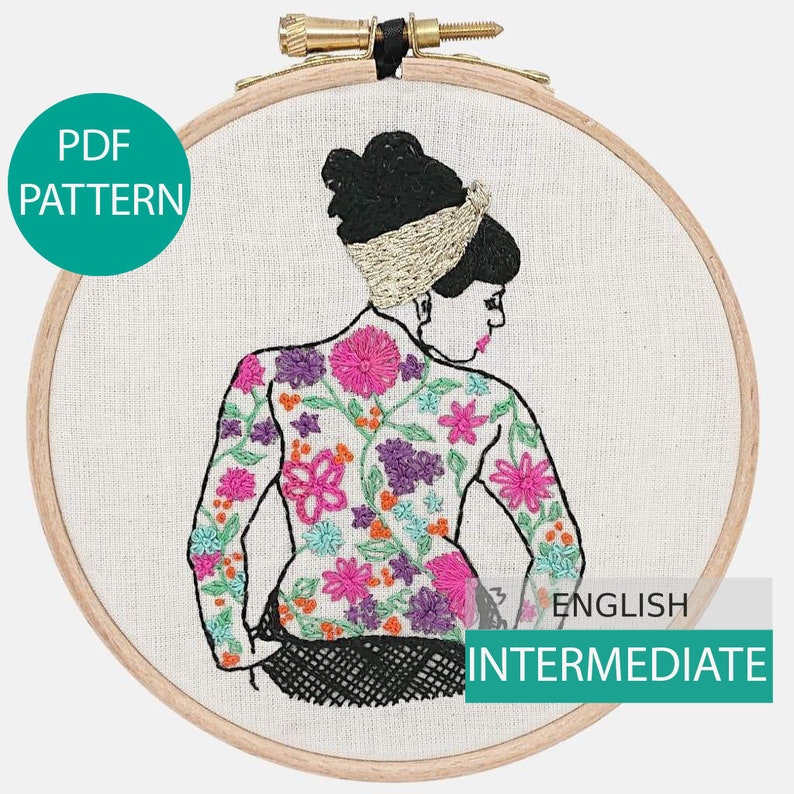 May include: Embroidered hoop art featuring a woman with a floral pattern on her back. The woman is wearing a gold headband and has black hair. The embroidery is done in a variety of colors, including pink, purple, orange, and green. The hoop is made of wood and has a diameter of approximately 8 inches. The text "ENGLISH INTERMEDIATE" is visible in the lower right corner of the hoop.