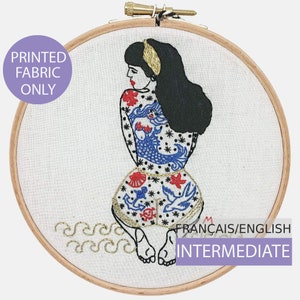 May include: Embroidery pattern featuring a woman with a blue and red tattoo on her back. The pattern includes a mermaid, stars, and other nautical elements. The pattern is labelled "FRANÇAIS/ENGLISH INTERMEDIATE".