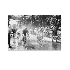 May include: A black and white photograph of a bicycle race with cyclists riding on a road. A banner overhead reads TOUR DE FRANCE L'EQUIPE. Spectators stand behind a fence along the side of the road while cyclists compete in the race.
