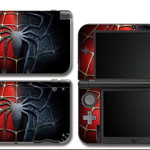 Może przedstawiać: Czarna konsola Nintendo 3DS z czerwono-czarnym wzorem pajęczyny. Wzór przedstawia dużego pająka pośrodku, z czerwoną pajęczyną po jednej stronie i czarną pajęczyną po drugiej.