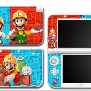 May include: Nintendo 3DS consoles featuring Super Mario Maker 2 designs. The consoles have red and blue backgrounds with Mario, Luigi, and other characters. The text "SUPER MARIO MAKER 2" is visible on the top of the consoles.