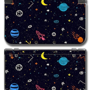 May include: A black Nintendo 3DS console skin featuring a colorful space-themed design. The design includes planets, stars, a crescent moon, a rocket ship, and other celestial elements. The skin covers the top and bottom of the console.