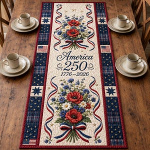 May include: Cream-colored table runner with a patriotic floral design. Features red poppies, blue flowers, and white daisies, with red, white, and blue ribbons. The text "America & 250 1776-2026" is displayed. Bordered by blue plaid and stars.