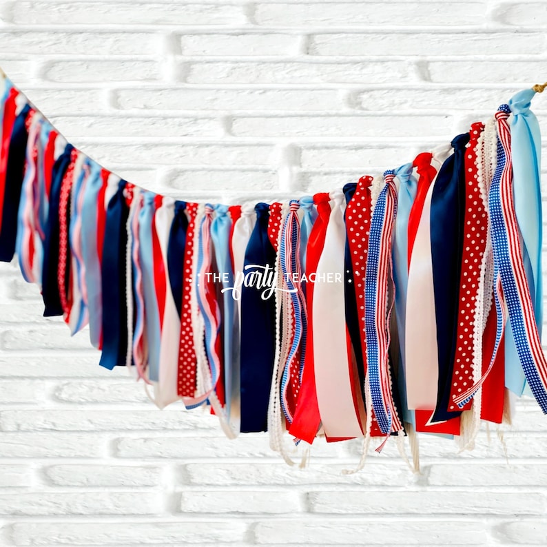May include: A red, white, and blue ribbon banner with a variety of patterns, including polka dots, stripes, and solid colors. The banner is hanging from a white brick wall. The text "THE party TEACHER" is visible on the banner.