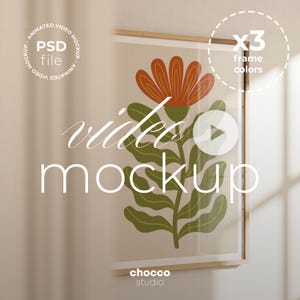 May include: A framed floral art print with a wooden frame. The artwork features an orange flower and green leaves on a beige background. The words "video mockup" are written on the print. The image also includes the text "PSD file" and "x3 frame colors".