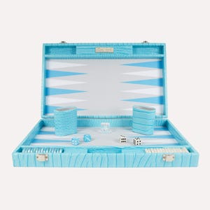 Puede incluir: Un juego de backgammon azul claro con un exterior texturizado. El tablero de juego abierto presenta un diseño azul, blanco y gris. Incluye dados, cubiletes y fichas. El juego se muestra sobre una superficie blanca.