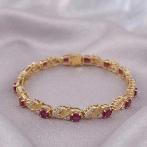 Könnte beinhalten: Ein goldenes Armband mit einer Reihe von oval geschliffenen roten Rubinen, die sich mit kleinen, klaren, rund geschliffenen Steinen abwechseln. Die Metallglieder haben ein strukturiertes, blattartiges Muster um jeden Rubin und einen Verschluss.