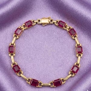 May include: A gold link bracelet featuring a series of rectangular, deep red gemstones set in polished gold frames. The bracelet is constructed with alternating metal links and stone settings, secured by a rectangular gold box clasp closure.