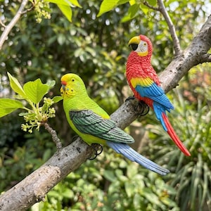 Pode incluir: Duas figuras coloridas de papagaios empoleiradas num galho de árvore. Uma é verde e amarela, a outra vermelha, amarela e azul. As aves são detalhadas com características realistas, ideais para decoração.
