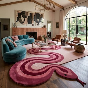 Puede incluir: Una alfombra grande con un diseño de serpiente estilizada en tonos rosa, magenta y rojo intenso. La alfombra tiene una forma corporal curva y alargada con una cabeza distintiva y una lengua bífida, colocada sobre un suelo de madera.