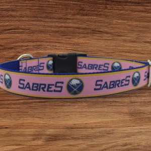 May include: Pink dog collar with a blue and gold Buffalo Sabres logo and the word "SABRES" repeated on the collar.