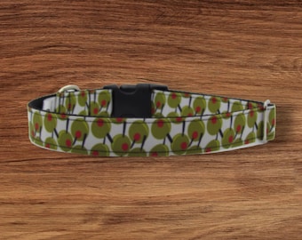 May include: A white dog collar with a green and red olive pattern. The collar has a black buckle and a silver D-ring.