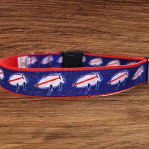 May include: A blue and red dog collar with a white buffalo design. The collar has a silver buckle and a black plastic slider.