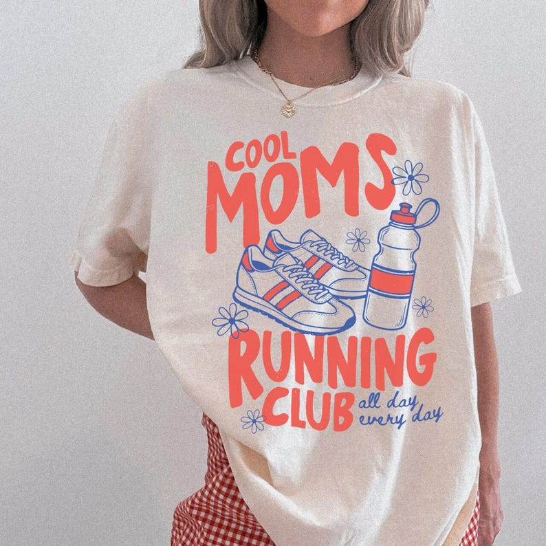 K&ouml;nnte beinhalten: Cremefarbenes T-Shirt mit dem Schriftzug "COOL MOMS RUNNING CLUB" in Koralle und Blau. Das Design umfasst Illustrationen von Laufschuhen, einer Wasserflasche und floralen Akzenten. Der Text "all day every day" ist ebenfalls enthalten.