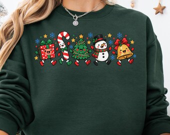 May include: A dark forest green crewneck sweatshirt featuring a graphic print of five animated Christmas characters: a gift box, a candy cane, a decorated pine tree, a snowman with a scarf, and a gold bell, all surrounded by small stars and snowflakes.