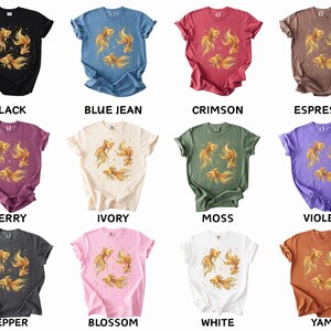 May include: A collection of short-sleeved t-shirts in various colors, each featuring a golden fish design. Colors include black, blue jean, crimson, espresso, berry, ivory, moss, violet, pepper, blossom, white, and yam. The shirts are casual wear.