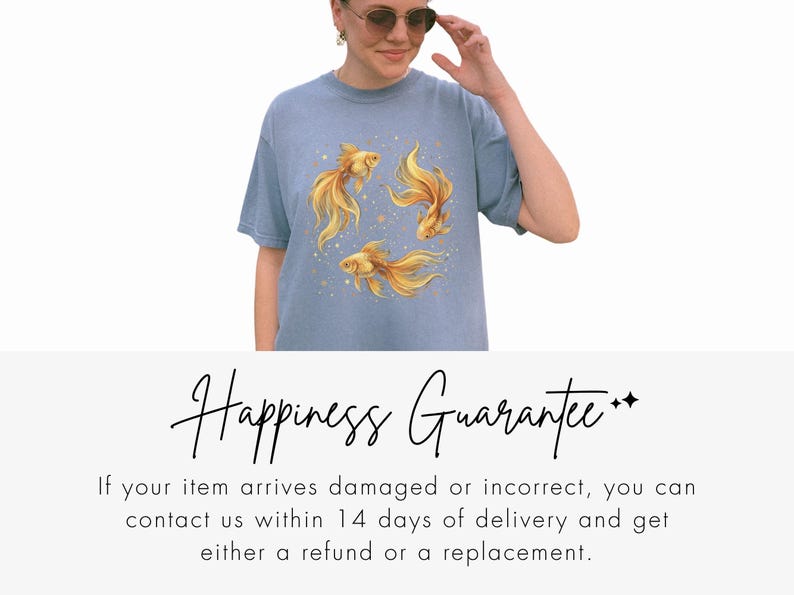 May include: A light blue t-shirt featuring a watercolor design of three golden goldfish. The fish have flowing fins and are surrounded by small gold dots. The shirt is a casual style.
