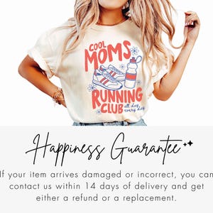 K&ouml;nnte beinhalten: Cremefarbenes T-Shirt mit dem Text "COOL MOMS RUNNING CLUB" in Rot und Blau, mit Laufschuhen und einer Trinkflasche. Das Shirt hat hochgekrempelte &Auml;rmel.