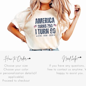 May include: Cream-colored t-shirt with the text "AMERICA TURNS 250 / I TURN 90" in navy blue, with two small American flags and the years 1776-1936-2026. The shirt is worn by a person.