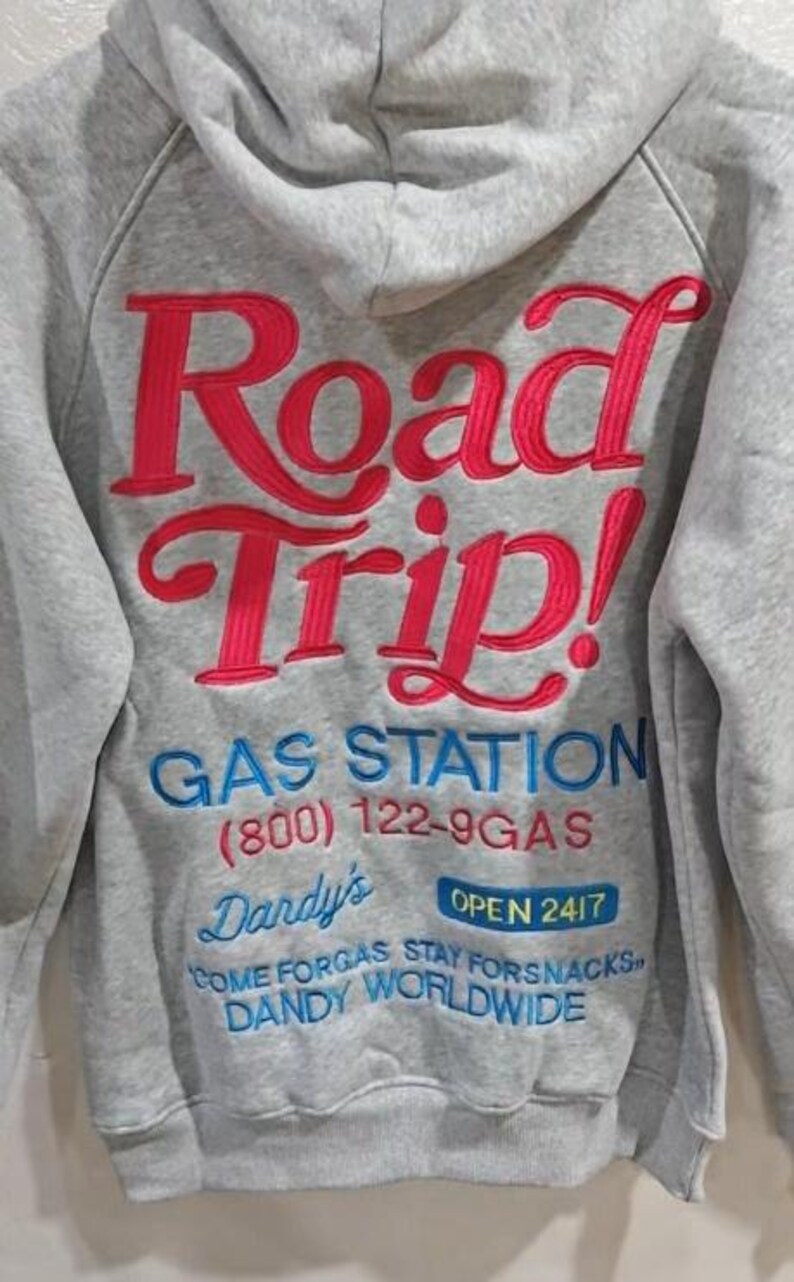 K&ouml;nnte beinhalten: Grauer Kapuzenpullover mit Stickerei. Auf der R&uuml;ckseite steht "Road Trip!" in Rot, dar&uuml;ber "GAS STATION" und weiterer Text in Blau. Der Hoodie hat einen l&auml;ssigen Stil.