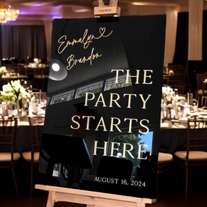 May include: Black acrylic sign with gold lettering on an easel. The sign reads "Emmelyn & Brandon The Party Starts Here August 16, 2024".