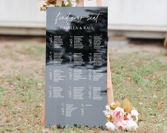 May include: Black acrylic wedding seating chart with white text. The chart is titled "find your seat" and "Camilla & Raul". The chart lists guest names by table number.