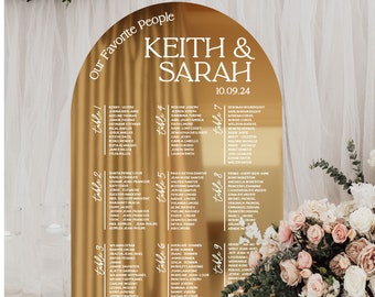 May include: Gold arch-shaped acrylic wedding seating chart with the names Keith & Sarah and the date 10.09.24. The chart lists guest names by table number.