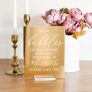 May include: Gold mirror acrylic sign with white text that reads "Blow bubbles of well wishes as we exit together as Mr. & Mrs. Please take one."