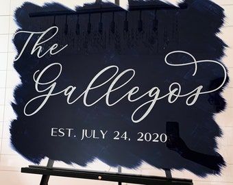 May include: A clear acrylic sign with a navy blue painted background and white lettering. The sign reads "The Gallegos Est. July 24, 2020". The sign is displayed on a black easel.