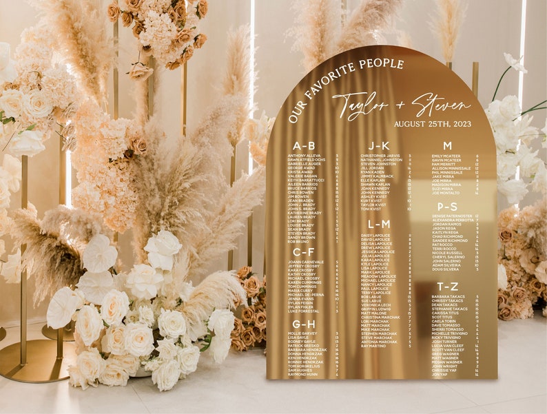 May include: Gold arch-shaped wedding seating chart with the text "Our Favorite People" and "Taylor + Steven" with the date "August 25th, 2023". The chart lists guest names alphabetically by last name.