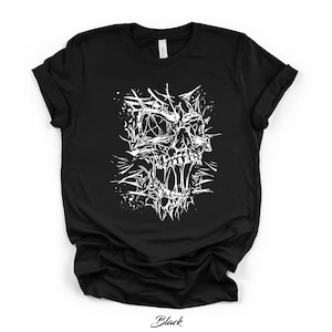 May include: Black t-shirt featuring a detailed white graphic of a skull with sharp, spiky elements. The skull has an open mouth and intricate detailing. The word "Black" is printed in cursive at the bottom.
