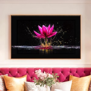 Könnte beinhalten: Gerahmter Kunstdruck mit einer leuchtend rosa Lotusblume vor schwarzem Hintergrund. Goldene und gelbe Akzente erzeugen einen Spritzeffekt um die Blume herum. Das Kunstwerk wird über einem rosa, getufteten Sofa mit dekorativen Kissen ausgestellt.