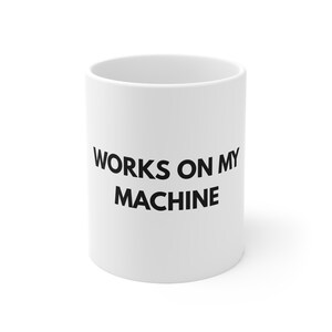 May include: White ceramic mug with the text "WORKS ON MY MACHINE" in black, centred on the front. The mug has a cylindrical shape and a simple design, suitable for coffee, tea, or other beverages.