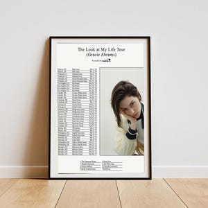 Op de afbeelding: Een ingelijste concertposter getiteld The Look at My Life Tour van Gracie Abrams. De poster bevat links een lijst met tourdata en locaties, rechts een portret van een persoon die de kin op de hand laat rusten, en een lijst met artiesten.