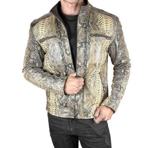 May include: A jacket featuring a snakeskin pattern in shades of beige, tan, and dark gray. The garment has a stand-up collar, a full-length front zipper, and two horizontal zippered chest pockets. It is worn over a solid black shirt.