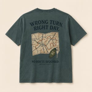 May include: A dark green short-sleeve t-shirt featuring a graphic on the back. The design includes a beige map with a red route, a green motel key tag labeled ROOM 08, and the text WRONG TURN. RIGHT DAY. NO ROUTE REQUIRED. SO:FAINT STUDIO.