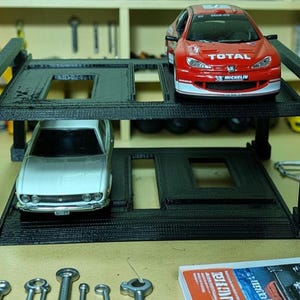 Può includere: Un garage per auto giocattolo nero a due livelli con un'auto da corsa rossa al livello superiore e un'auto argentata sotto. Il garage ha ritagli rettangolari. Sono visibili strumenti e altre auto giocattolo.