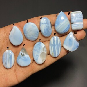 Könnte beinhalten: Zehn polierte blaue Opal-Cabochons, beschriftet mit den Nummern eins bis zehn. Die Steine haben verschiedene Formen wie Tropfen, Ovale und ein Rechteck und zeigen milchig blaue und weiße Wirbelmuster mit glatten, reflektierenden Oberflächen.