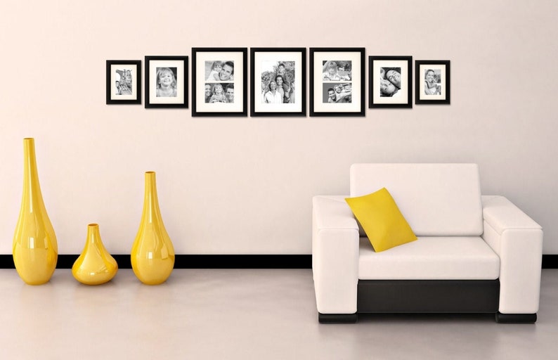 May include: A white couch with a yellow pillow sits in front of a white wall with six black picture frames containing black and white photos. Three yellow vases of different sizes are on the floor in front of the couch.